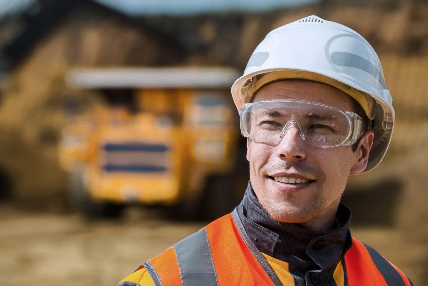 Surface mine worker wearing a hard hat, safety glasses and hi-vis vest in front of a haul truck